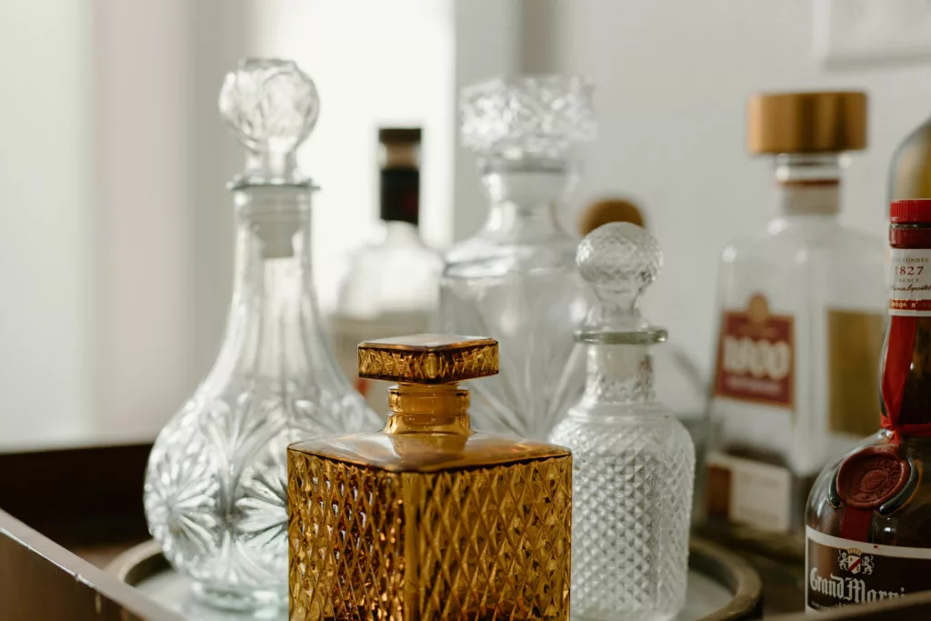 An array of decanters and bottles on a tray, with a focus on a golden amber tequila decanter at the forefront. The decanter has a textured pattern and is capped with a matching golden stopper.