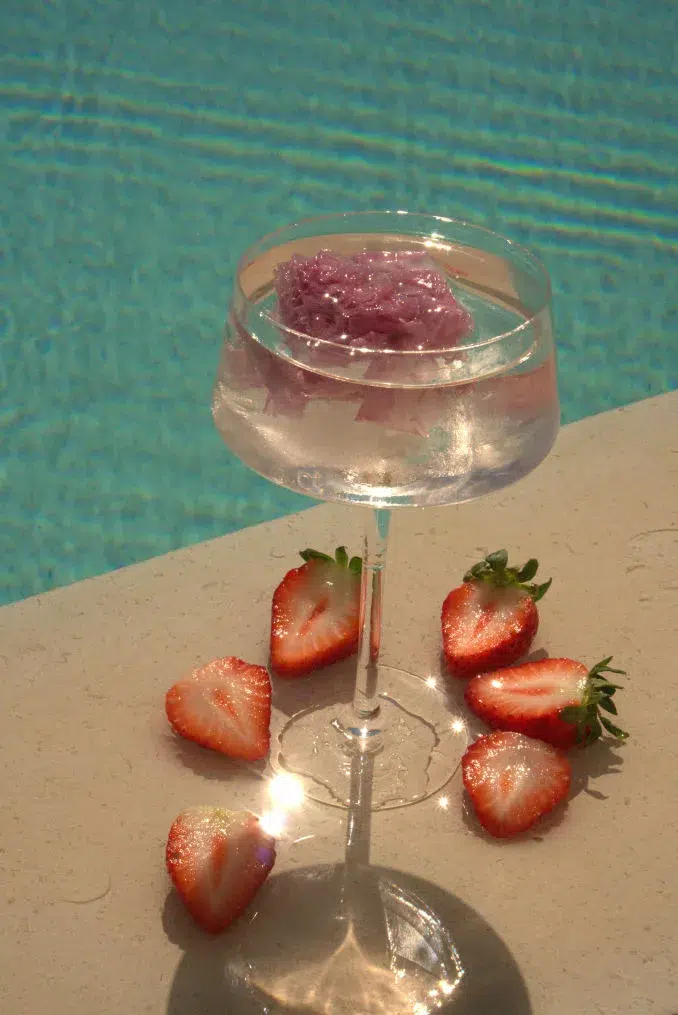 A glass of tequila on the rocks with a garnish of strawberries by a sparkling pool, showcasing a refreshing flavored tequila experience.