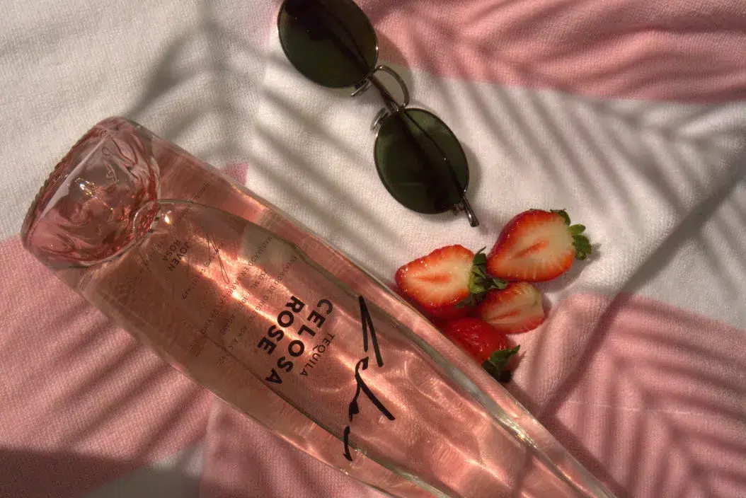 A bottle of Celosa Rosa Tequila with fresh strawberries and sunglasses, embodying a summer flavored tequila vibe.